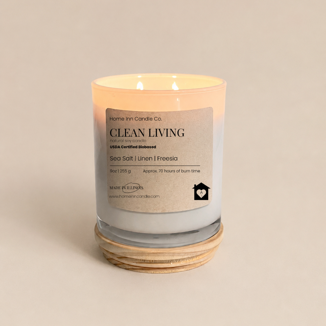 A lit double-wick candle in a white glass jar with a cream label reading 'Clean Living' from Home inn Candle Co. 