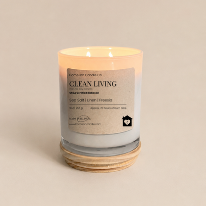 A lit double-wick candle in a white glass jar with a cream label reading 'Clean Living' from Home inn Candle Co. 