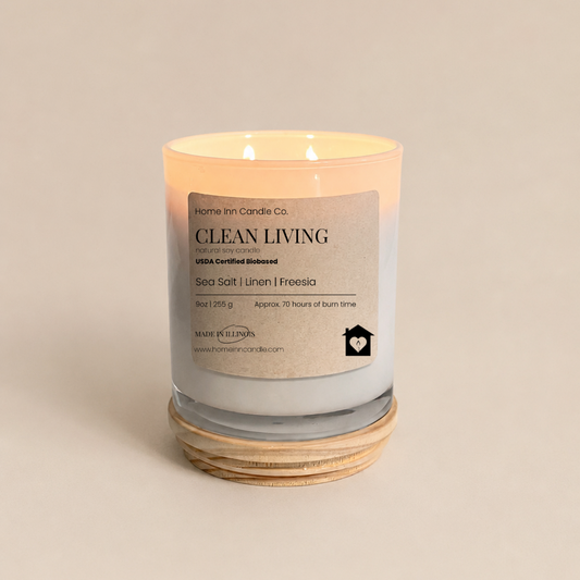 A lit double-wick candle in a white glass jar with a cream label reading 'Clean Living' from Home inn Candle Co. 
