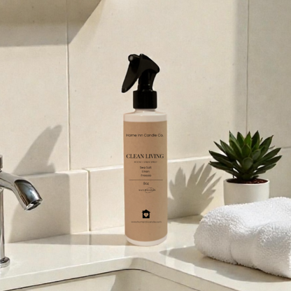 Room Spray Labeled Clean Living by Home Inn Candle on a bathroom counter with sink and towel in the background