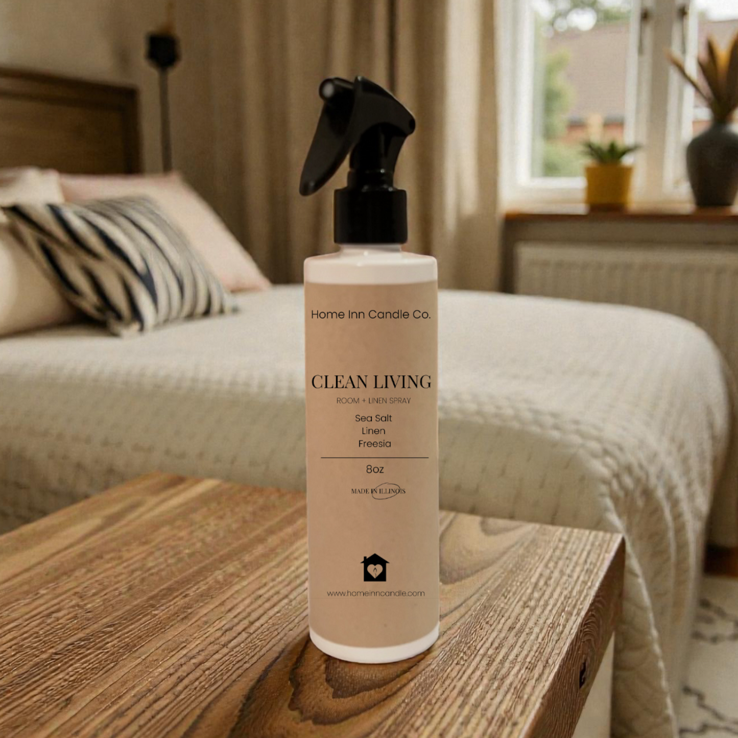 Home Fragrance room spray bottle labeled 'Clean Living' by Home Inn Candle on a wooden surface with a bedroom in the background