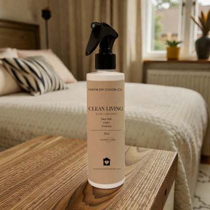 Home Fragrance room spray bottle labeled 'Clean Living' by Home Inn Candle on a wooden surface with a bedroom in the background