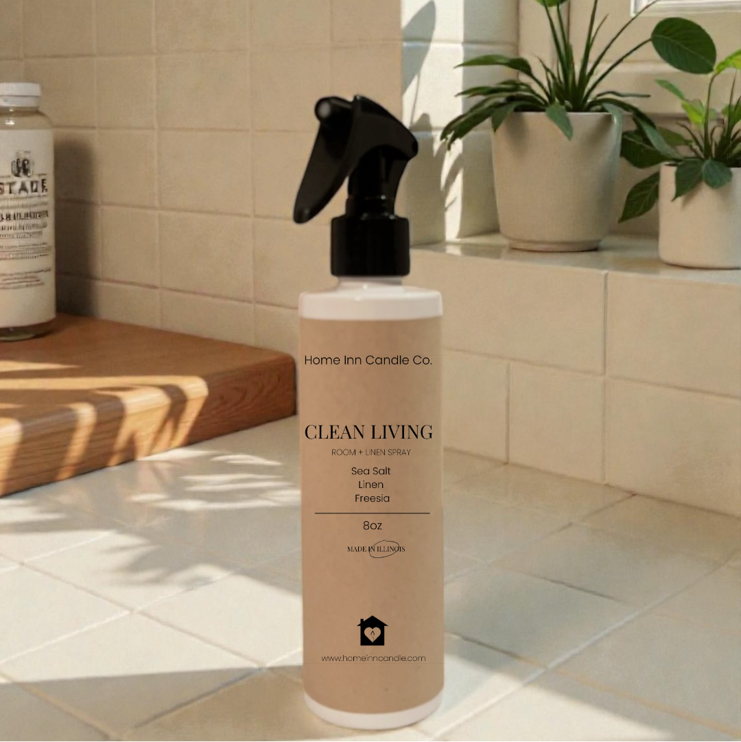 Bottle of 'Clean Living' room spray by Home Inn Candle on a kitchen counter with plants and a window in the background.