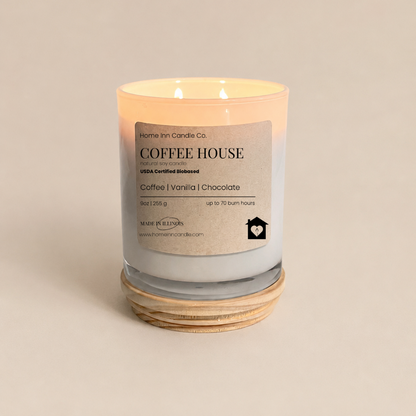A lit double-wick scented candle in a clear glass jar with a beige label reading 'COFFEE HOUSE' and 'Coffee | vanilla | Chocolate.' from Home Inn Candle