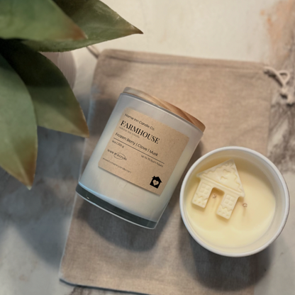 Candle labeled 'Farmhouse' from Home Inn Candle next to a small bowl with a house-shaped candle on a marble surface.