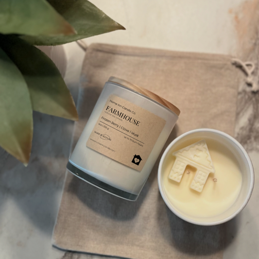 Candle labeled 'Farmhouse' from Home Inn Candle next to a small bowl with a house-shaped candle on a marble surface.