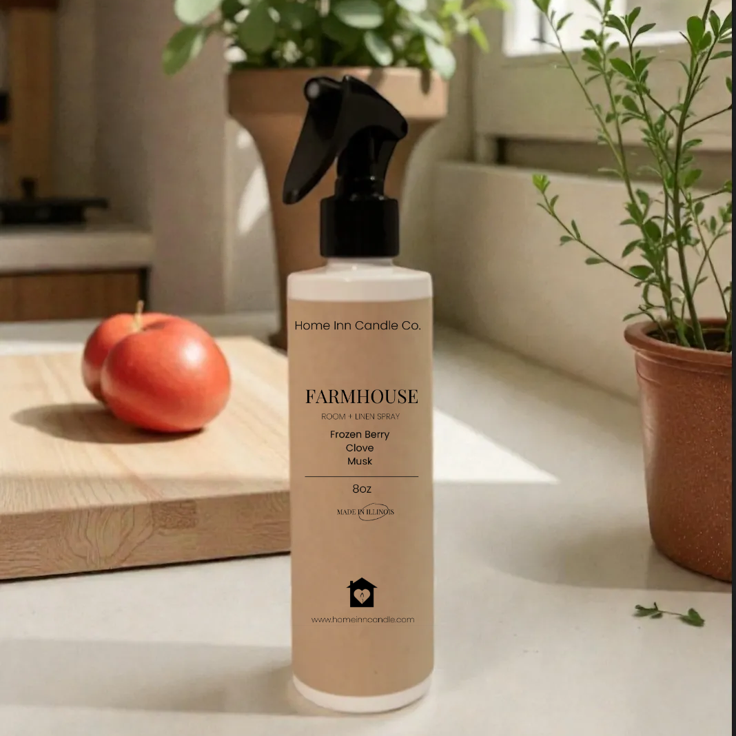 Bottle of Farmhouse Room spray by Home Inn candle on a surface with plants and an apple in the background
