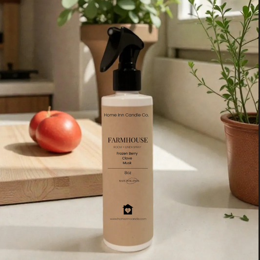 Bottle of Farmhouse Room spray by Home Inn candle on a surface with plants and an apple in the background