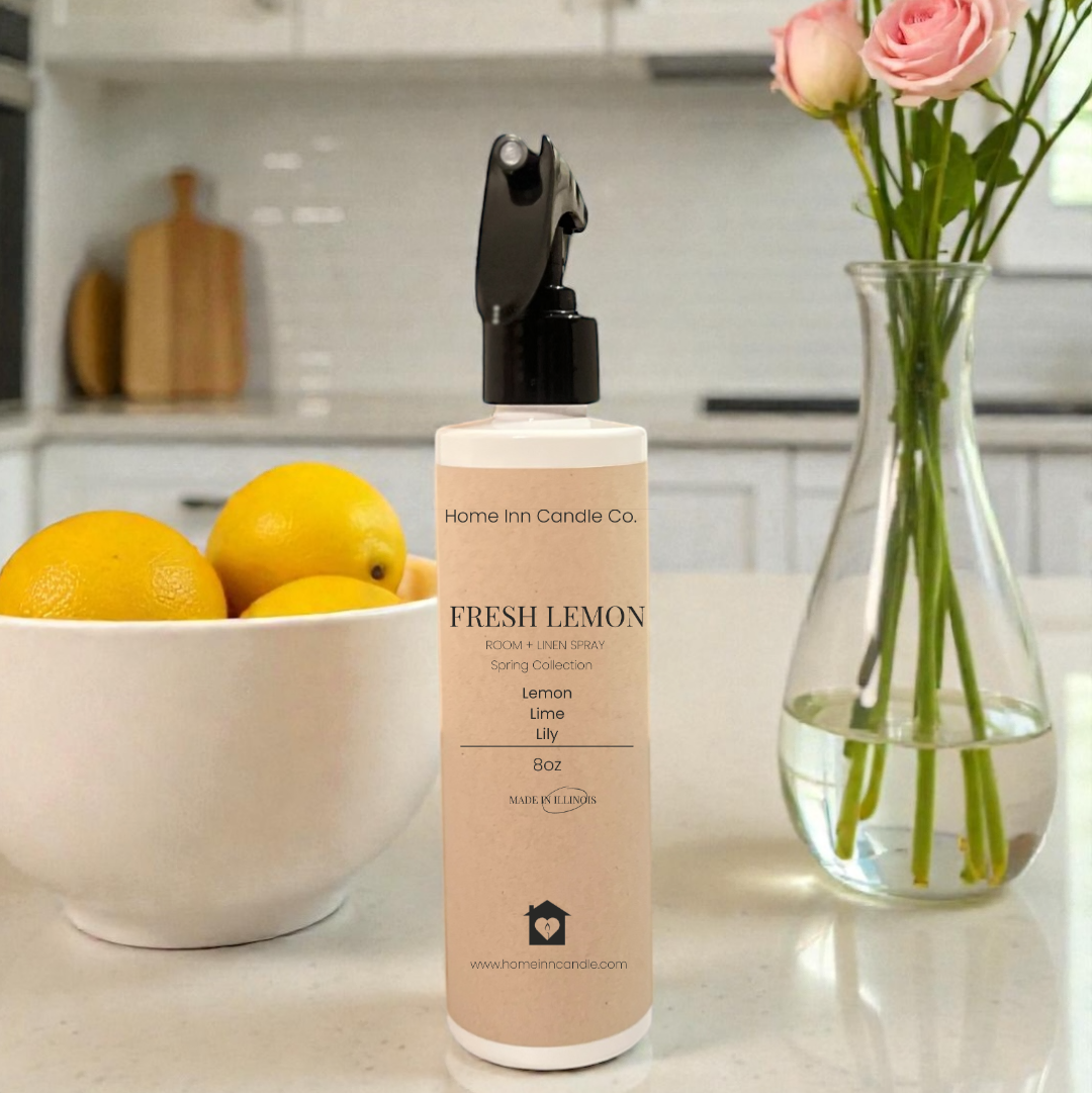 Fresh Lemon room spray from Home Inn Candle co on kitchen counter with fruit bowl of lemons and pink floral arrangement in a vase. 