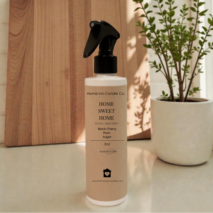 Room Spray bottle labeled 'Home Sweet Home' by Home Inn Candle on a kitchen counter with a cutting board and plant in the background.