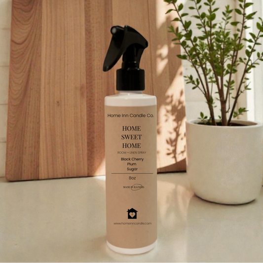 Room Spray bottle labeled 'Home Sweet Home' by Home Inn Candle on a kitchen counter with a cutting board and plant in the background.