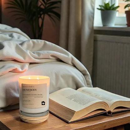 Candle and open book on a wooden table near a window with plants in the background