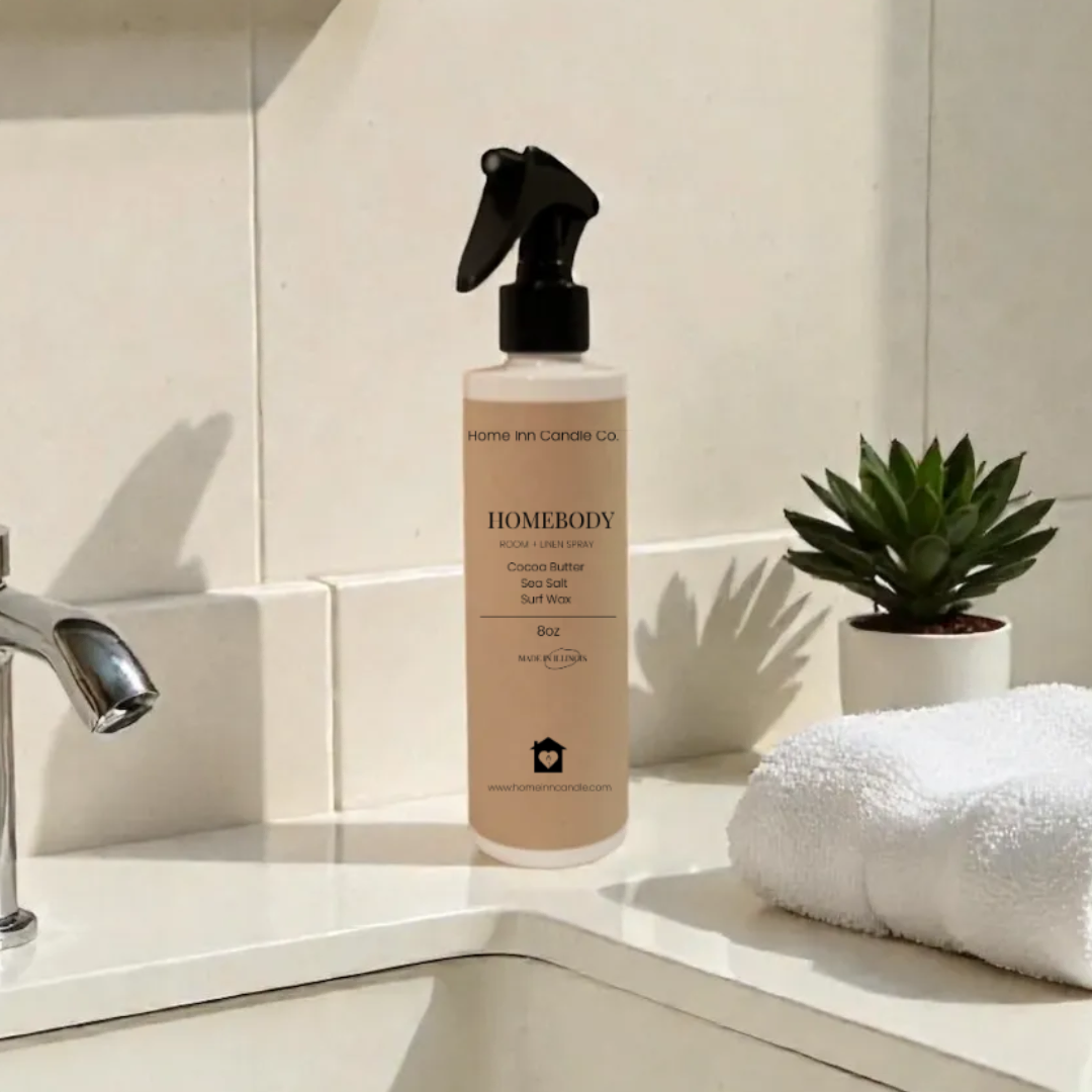 Homebody Room Spray by Home Inn Candle on a bathroom counter with sink and towel in the background