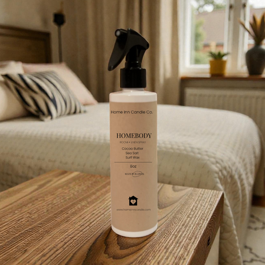 Homebody room spray by Home Inn Candle  on a wooden surface with a bedroom in the background