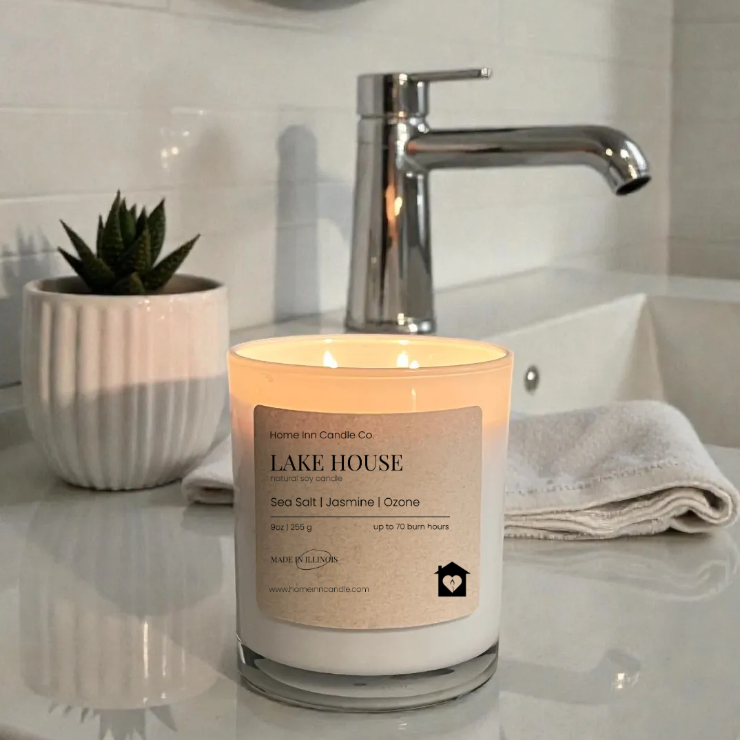 Candle labeled 'Lake House' on a bathroom counter with a mirror and faucet in the background.