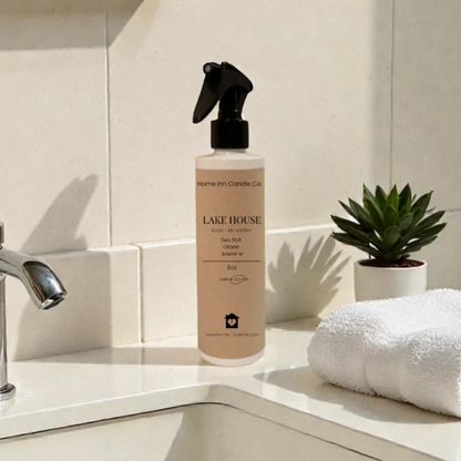 Room Spray bottle labeled Lake House by Home Inn Candle on a bathroom counter with sink and towel in the background