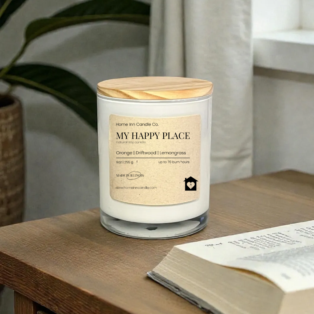 Candle labeled 'My Happy Place' on a wooden surface with an open book and plant in the background