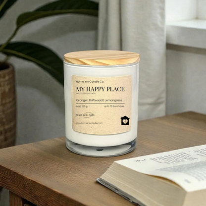 Candle labeled 'My Happy Place' on a wooden surface with an open book and plant in the background