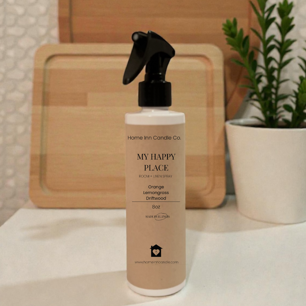 Bottle of 'My Happy Place' spray from Home Inn Candle on a surface with wooden boards and a plant in the background.