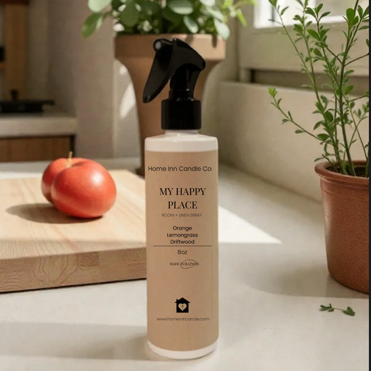 Bottle labeled 'My Happy Place' from Home Inn Candle on a surface with plants and an apple in the background