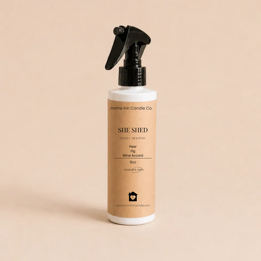 A bottle of She Shed Room spray from Home Inn Candle with a black trigger sprayer and a beige label, set against a solid beige background.