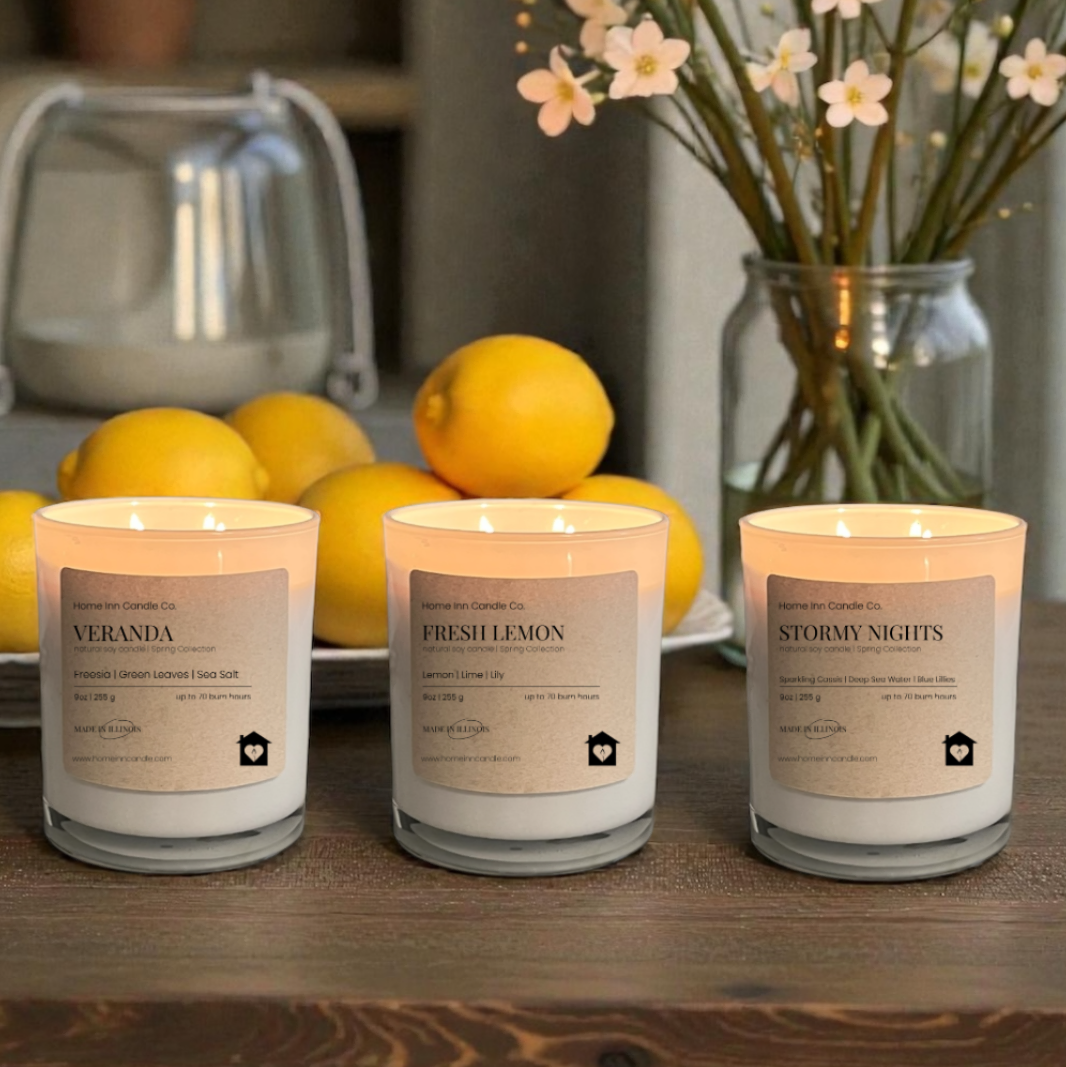 Three candles labeled Fresh Lemon, Veranda, and Stormy Nights from Home Inn Candle Company on a wood table with fruit and floral decor