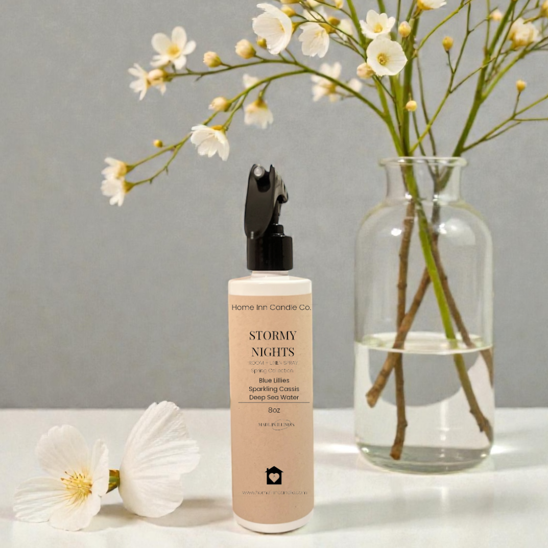 Stormy Nights room spray from Home Inn Candle Co on a white surface with a floral arrangement in a vase