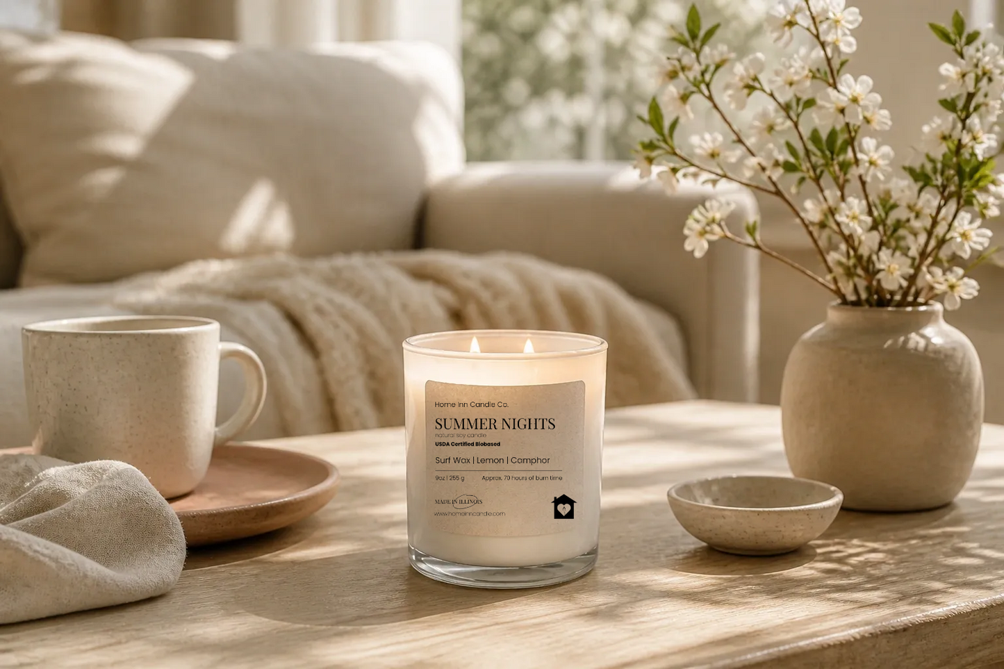 Candle labeled 'Summer Nights' on a table with a mug, vase, and flowers in a cozy living room setting.Home Inn Candle