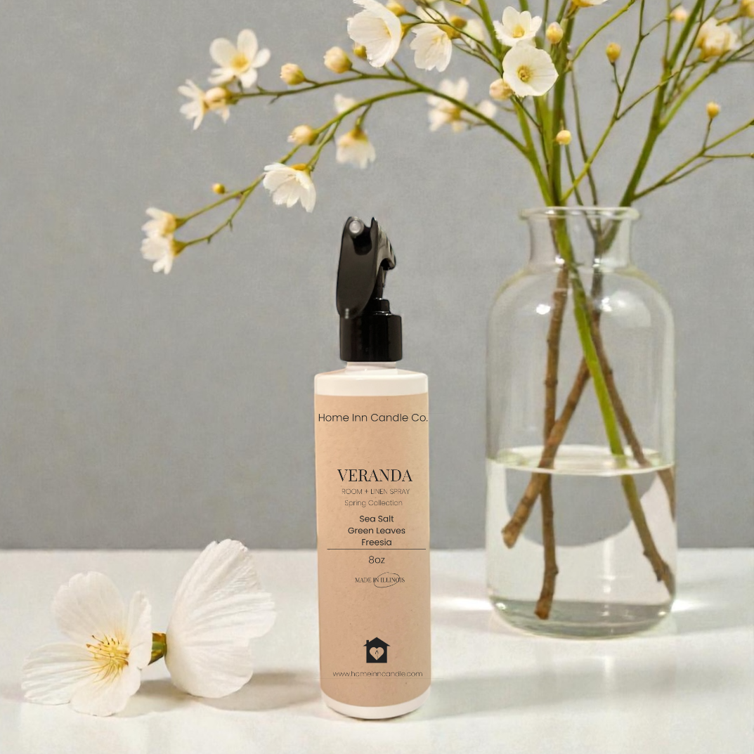 Veranda Room Spray bottle on white surface with floral arrangement in a glass vase