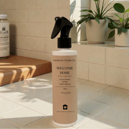 Bottle of 'Welcome Home' room spray by Home Inn Candle on a windowsill with plants and a tiled wall in the background
